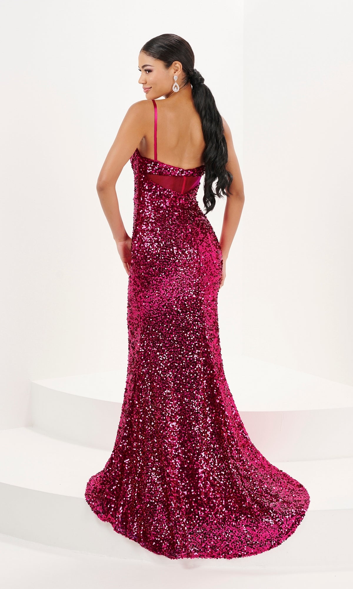 A woman stands on white steps wearing the Tiffany V-Neck Fitted Long Sequin Prom Dress 16081—a floor-length pink gown with thin straps, open back, and styled with her long dark hair in a ponytail.